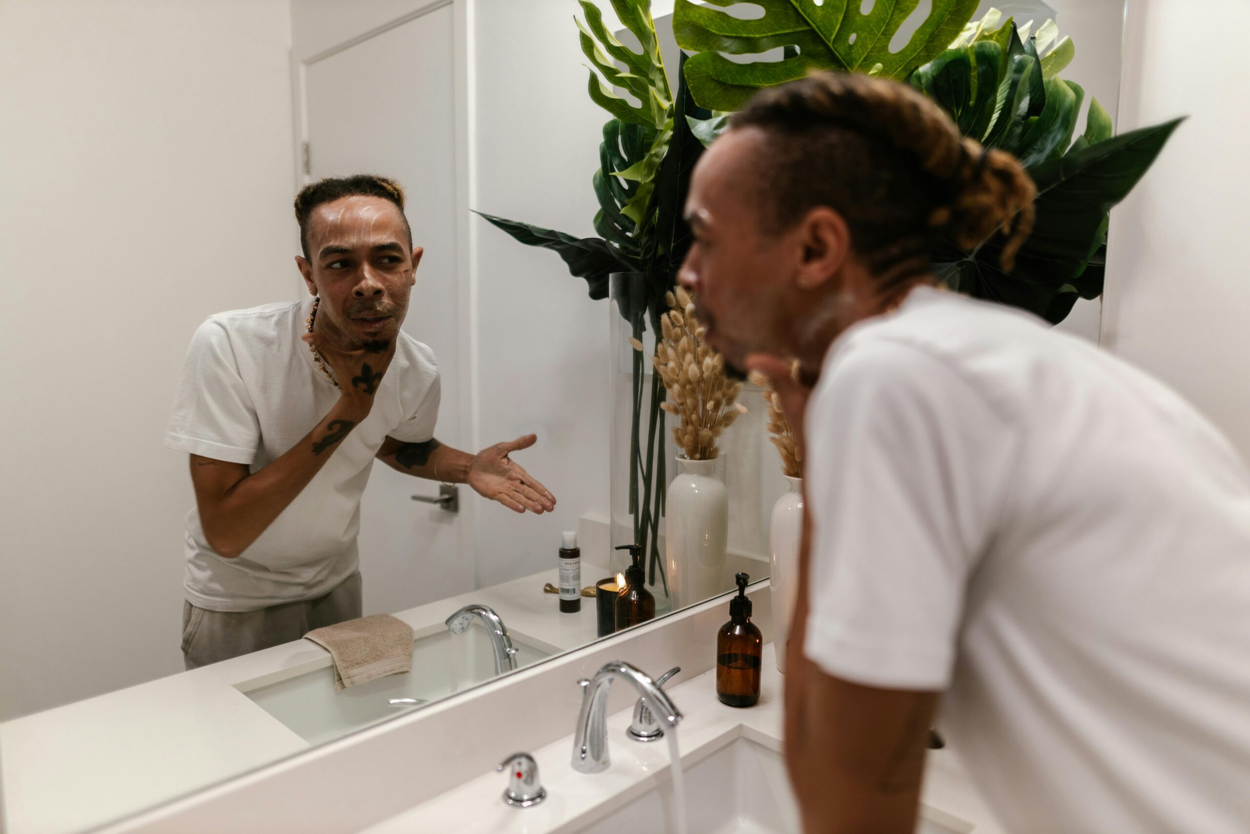 Young Man Looking in Mirror Washing at Bathroom Sink