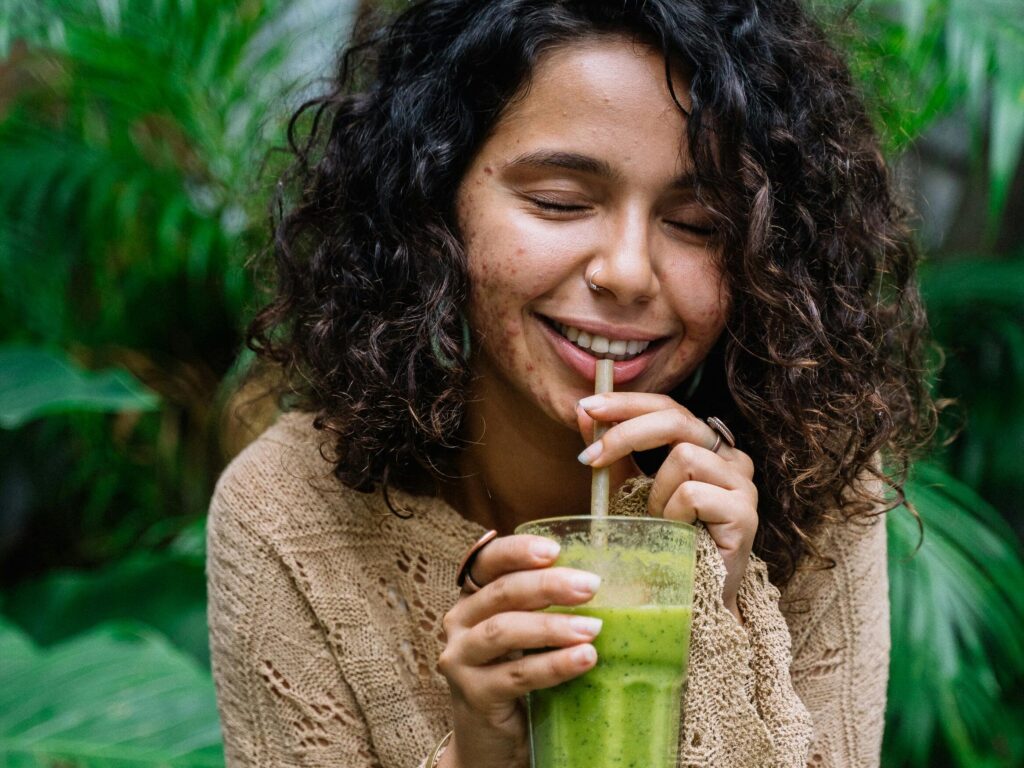 mujer con acné bebiendo un jugo verde.